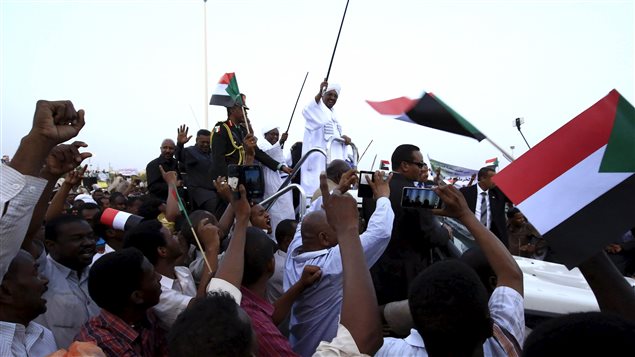 الرئيس السوداني عمر البشير يلوّح بيديه لمناصريه في مطار الخرطوم لدى عودته من  مؤتمر القمّة الافريقي في جوهانسبورغ في 15 حزيران يونيو 2015