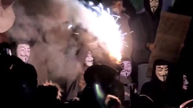 Protesters with Guy Fawkes masks are illuminated by flares in this screengrab from a YouTube video posted from an Anonymous-affiliated account. Anonymous, a cyber vigilante group, took credit for Wednesday's attack on federal government computers. We see a hal-dozen persons dressed in black robes and wearing masks that feature wide pencil-thin moustaches with a third moustache down the chin. One of the men is holding a brightly lit flare that dominates much of the picture. Surrounding the men are billowing smoke clouds.