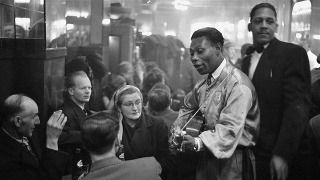 Au bar du rez-de-chaussée du Rockhead's Paradise, le célèbre chanteur calypso, Lord Caresser, visite des tables bondées, 1951. Au bar du rez-de-chaussée du Rockhead's Paradise, le célèbre chanteur calypso, Lord Caresser, visite des tables bondées, 1951.