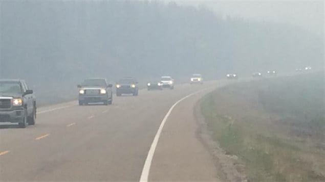 Des véhicules partent de La Ronge, en Saskatchewan au milieu de la brume des feux de forêt. Ceux qui ne peuvent pas sortir par leurs propres moyens sont transportés en autobus par le gouvernement. (Gouvernement de la Saskatchewan).