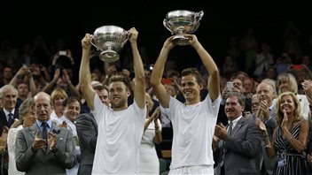 Pospisil, right, and his American doubles partner, Jack Sock, hold up their trophies after defeating Bob Bryan and Mike Bryan of the U.S in the men's doubles final last year at Wimbledon. We see two fit young blond men holding trophies over their heads and smiling wildly.