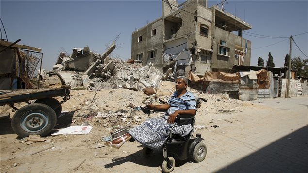 أستاذ الرياضيات الفلسطيني علي وحدان يمر في كرسيه المتحرك الكهربائي أمام أنقاض منزله في بيت حانون في شمال شرق قطاع غزة في 6 تموز (يوليو) الجاري. يقول شهود عيان إن القصف الإسرائيلي  دمر المنزل في حرب الصيف الفائت. ولم تقتصر الأضرار على الممتلكات، إذ فقد وحدان زوجته و11 فرداً من عائلته وإحدى ساقيْه خلال القصف الإسرائيلي. وبعد مرور نحو سنة على ذلك قرر الأطباء بتر ساقه الثانية.
