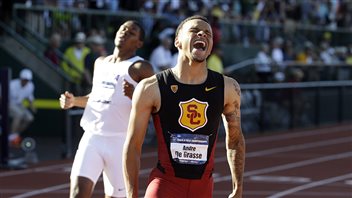Pan Am organizers are hoping Canadian sprinter Andre De Grasse will excel, prompting people to abandon their televisions to show up in person. We see a tan-skinner man with his mouth agape in joy after winning a race. He is wearing a back-and-white sprinters outfit with SC (for the University of Southern California) printed on his jersey and his name on one of those i.d. tages that track people wear. The second place finisher is pulling up behind him.