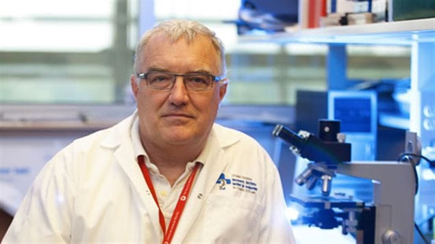 John Bell is leading a team in a new fight against cancer. We see Dr. Bell in his lab in a labcoast. Behind him are microscopes and computer screens. He appears to be about 60 with white hair and is wearing glasses.
