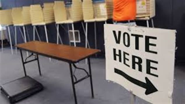 Its creators hope the new Vote Note app will get more youth out to the polls. We see an empty table with chairs in the background. To the right of the picture in a sign that says "Voter Here." An arrow under the words is pointing to the right.