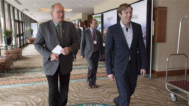 Are P.E.I. Premier Wade MacLauchlan, left, and New Brunswick Premier Brian Gallant heading to an agreement on a national energy strategy this week?  We see two men walking down a hotel corridor. Gallant, young and handsome, is wearing a dark suit, stripped shirt and no tie. His light bron hair is parted on the left in something of a Oxbridge style, overflowing just a touch on his forehead. Mr. MacLauchlan is older and somewhat frumpier. He wears glasses under receding grey hair. He wears a grey sports jacket, stripped tie and brown pants. He carries a piece of paper in his right hand. In the background is an identified man. Further back we see some men exiting a door. It appears likely that all have just left a meeting.