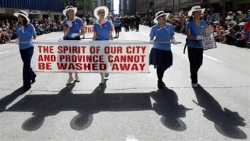 The 2013 Calgary Stampede parade went on as planned in the wake of devastating floods that hit Alberta in the weeks leading up to the annual event.   More than a million people attend the Stampede every year. We see five women dressed in blue shirts and white cowboy hats holding a white banner that written in red says, 