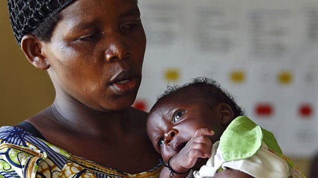 At least 3.2 million children around the world suffer from HIV/AIDS. We see a black woman dressed in a colourful African dress cradling a child in her arms. The mother is looking at her child with concern. The child's eyes are gazing off into the distance.