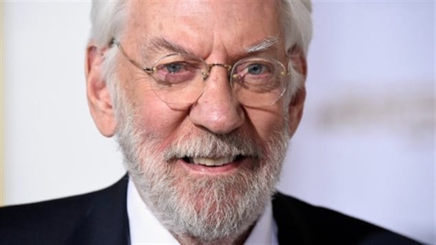 Donald Sutherland is not happy with voting restrictions on Canadians living abroad. We see a closeup of Mr. Sutherland's face. He is wearing rimless glasses, has a short, white beard and his half smiling as he appears to be listening to a question.