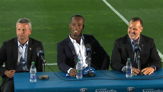 L'attaquant Didier Drogba, au centre, en compagnie de l'entraîneur-chef de l'Impact, Frank Klopas (à gauche), et du président de l'équipe, Joey Saputo (à droite).