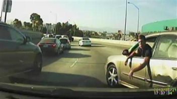 It doesn't take a lot to set off a case of road rage. We see a man sticking his head outside the window of his light-coloured car, which appears to be stopped on a highway. Both his arms are hanging over his driver's side door. To his left, a line of cars passes him in the passing lane.
