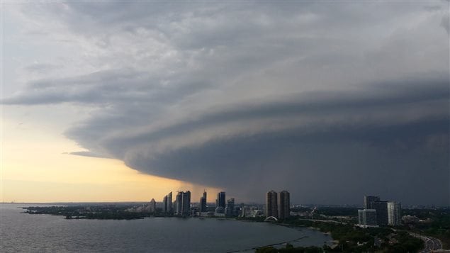 A major storm cloud passes over Etobicoke, a former municipality that is now a part of western Toronto, on Sunday evening. We see the buildings of Etobocoke from across some dark water. Overhead is a dark, menancing cloud that fills most of the sky in the photo. To the left, we see pale, yellow sky.