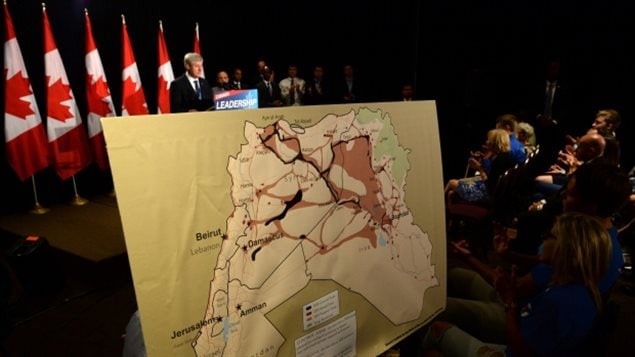 Stephen Harper montrant une carte des zones contrôlées par les terroristes en Syrie et en Irak qui seraient donc probablement parmi les endroits où il interdirait les Canadiens à voyager s’il est réélu. (Sean Kilpatrick / Presse canadienne)