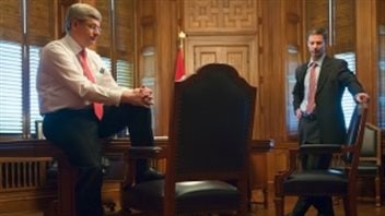 Stephen Harper, left, and his chief of staff, Nigel Wright, on Parliament Hill in an undated photo. We see Harper dressed in dark pants, dress shirt and tie done up (no jacket) leaning backwards against a desk with his right foot on the floor and left left foot planted on a very plush wooden chair with a dark cushion. His hands are clasped over his left knee. Wright is to the right wearing a grey suit with tie done up. He rests his left hand on the back of a plush chair. His right hand rests on his right hip.