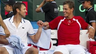 Daniel Nestor, left, and Vasek Pospisil could be playing together at next year's Rio Olympics. Nestor is white and Pospisil in a red shirt sit on a bench with wide smiles. They are looking at each other and bumping fists in celebration.