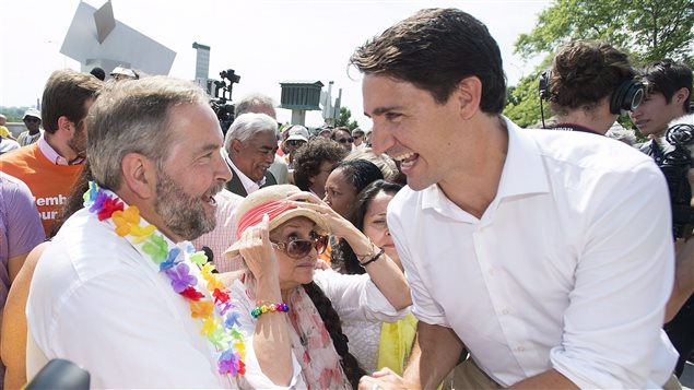 Liberal leader Justin Trudeau, left, and Bloc Quebecois Leader Gilles Duceppe wave to supporters during Sunday's annual gay pride parade in Montreal, Sunday. NDP leader Tom Mulcair and Green Party leader Elizabeth May also attended while Stephen Harper campaigned in Ottawa. Duceppe, who is developing a paunch, wears a blue dress shirt with the sleeves rolled up just a tad. He holds gay pride flag high with his right hand. In his left hand is a small plastic water bottle. He wears dark pants and has a pair of sun glasses tucked into the top of his shirt. Trudeau in a white shirt and brown pants, is looking into the distance. If it were theatre, he would be playing the gods.