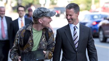 Kerry Kolodiazny, a member of the public following the trial, left, uses his laptop to film himself with Nigel Wright, as he leaves the courthouse in Ottawa on Monday. We see Kolodiazy dressed in a flowered sports coat right out of the 1960s with a hat to match, holding his computer as he leans in to address Mr. Wright, who, as usual, is dressed in a fancy, dark suit and tie. Mr. Wright is smiling broadly.