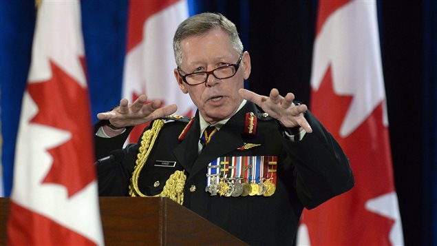 Gen. James Vance issues order banning sexual misconduct in the Canadian military. We see the general standing at a podium with three Canadian flags in the background. His dark glasses are lowered on his nose. His dark uniform is filled with medals against his left chest and braiding over his right shoulder. He is looking out at an audience and gesturing with his left hand raised.