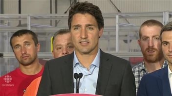 Liberal leader Justin Trudeau cut Ala Buzreba some slack for comments she made four years ago on Twitter. We see Trudeau in a photo op shot, wearing a dress shirt and no tie and a brown sports jacket. Behind him are four men, all of whom appear to be in their 30s. They all have short hair. Two have light beards. Three are wearing just shirts while the fourth wears a blue sports jacket.