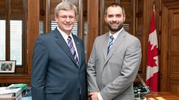 Stephen Harper, left, and former PMO lawyer Benjamin Perrin are seen in happier times. Harper is seen in a blue-grey suit that covers a growing paunch. Perrin wears a light-coloured suit and appears to be in excellent shape. Both men are looking at the camera with something resembling silly grins on their faces. Perrin has a dark beard, Harper is clean-shaven.
