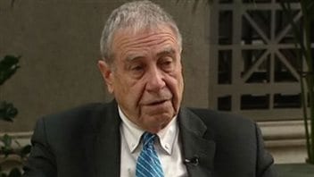 Bruce Carson, a former senior adviser to Prime Minister Stephen Harper, is under investigation over allegations he illegally lobbied his former government colleagues. His trial began Monday. Carson is seated and looking pensive with his face slightly turned down. He wears a grey sports jacket, oxford shirt and blue tie. He is likely being interviewed as a tiny mic sits on his left lapel.