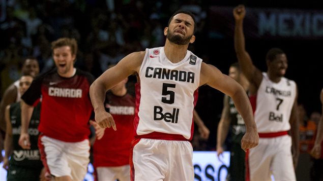 Cory Joseph celebrates his winning basket in Canada's 87-86 victory over Mexico Saturday at the FIBA Americas Championship third place basketball game in Mexico City. A one-point loss Friday to eventual champion Venezuela, prevented Canada from advancing to the Rio Olympics. They have one more chance next summer. We see Joseph, a tall, bearded, black man, spreading both arms in celebration with his eyes closed tight. He wears a white uniform with Canada, the number five, and Bell printed in black on the front of his uniform. Behind him, we see his teammates--in both warmup jackets and in uniform--joining the celebration. All have wide smiles on their faces.