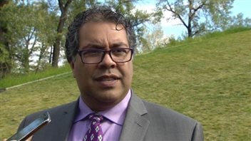 Calgary Mayor Naheed Nenshi says he wishes the city had made a bid for the 2022 Olympic Winter Games, and he confirms he has been part of conversations about the possibility of making a bid for the 2026 Games. We see a man of south-Asian complexion. He wears large glasses and a grey suit with a blue dress shirt and fancy tie. He is standing in front of a grassy mound and is appears to be listening to a question.