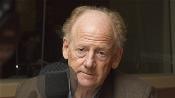 John Ralston Saul, a Canadian, is president of PEN International. We see Mr. Saul sitting behind a microphone. Balding but still retaining much of the blond in his hair, his face is deeply lined with babs under his eyes. He has something of a sad look on his face.