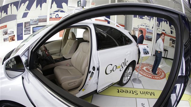 Ontario announced Tuesday it will allow road tests on self-driving cars (photo) beginning next year. We have a fancy shot through a wide driver's side window of a white, rounded vehicle that has a beige interior that pretty much looks like any other car interior. On the back door the word "Google" is written. However, in place of the second "o" in Google, is a drawing of the front of rounded car that pretty much looks the the real car on whose door it sits. The car sits in a fancy showroom.