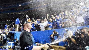 Toronto third baseman Josh Donaldson sprays champagne on fans in the wake of the Jays' series victory on Wednesday. We see Donaldson wearing googles and a dark championship tee-shirt with his mouth wide open in a shout spaying bubbles high into the air on fans in the stands and members of the press corps.