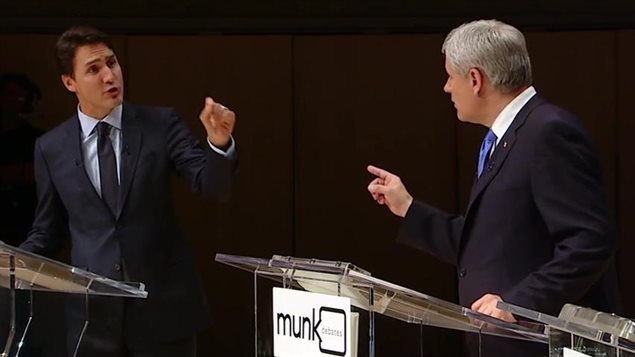 Justin Trudeau, left, and Stephen Harper exchanged sharp words over citizenship at a leaders' debate in Toronto in September. We see Trudeau in the left of the photo with his left arm raised pointing at Harper, who is pointing back with his right hand. Harper stands behind a podium with the words "Munk Debates" written in front. Both are wearing sharp, dark suits. Trudeau appears trim. Harper looks paunchy. Trudeau, his dark hair styled and parted on the right, looks young. Harper wears his grey hair flattened over, parted on the left.
