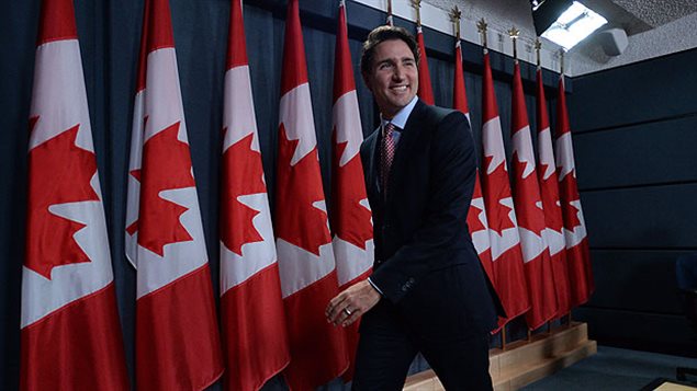 Justin Trudeau was all smiles after meeting the media on Tuesday. We see a lithe man in a dark suit in full stride with a wide smile leaving the press room. Behind him are about dozen red and white Canadian flags.