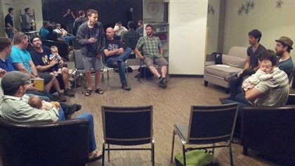 Fathers meet at a so-called Boot Camp for New Dads in Saskatoon in 2012. A new study indicates that a significant number of expectant fathers suffer some symptoms of depression. We see a group of men gathered in something of an unwieldily circle. Most are dressed very casually. Three of them are holding babies. Except for the presence of the babies, the gathering could be, perhaps, a 12-step program meeting, such as Alcoholics Anonymous. It appears to be taking place in one of those non-descript meeting rooms located in many hospitals with its collection of armless chairs and tacky sofas.