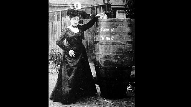 Annie Taylor poses in a backyard with a barrel and her hand on the cat, presumably which now has only 8 lives after surviving the 