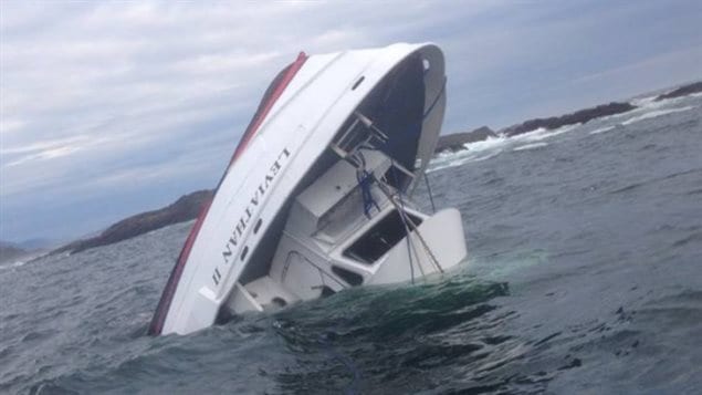 The MV Leviathan II capsized on Sunday. We see the white prow of the boat facing up toward the blue sky at about an 70 per cent angle. It is submerged to its wheelhouse and surrounded by dark purple water.