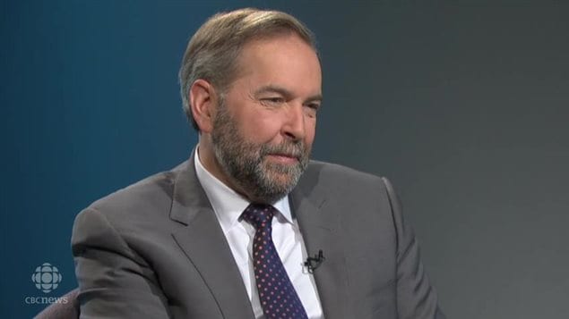 Tom Mulcair makes no apologies for niqab stand.We see the bearded and neatly coiffed Mulcair from the middle of the chest up. He wears a soft grey suit, white shirt and dark tie. He appears to be listening to a question and wears a gentle look on his face.
