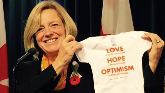 Alberta Premier Rachel Notley holds up a onesie for the expected baby of an elected representative.