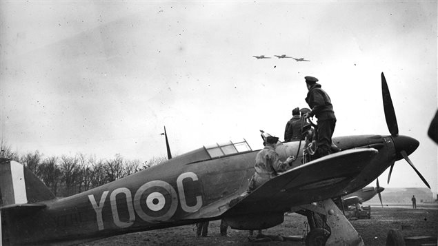 A Hurricane is re-armed while a section flies overhead. From the photo album of Flying Officer R.W.G. Norris, from Saskatoon, Saskatchewan, who served with No. 1 Squadron during the Battle of Britain. IT was this type of fighter that Gill was piloting when attacked by four Japanese fighters and shot down and killed in 1943.