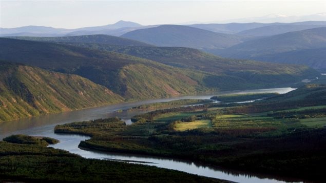 A river is shown snaking through green, mountainous terrain on a sunny day in Yukon.