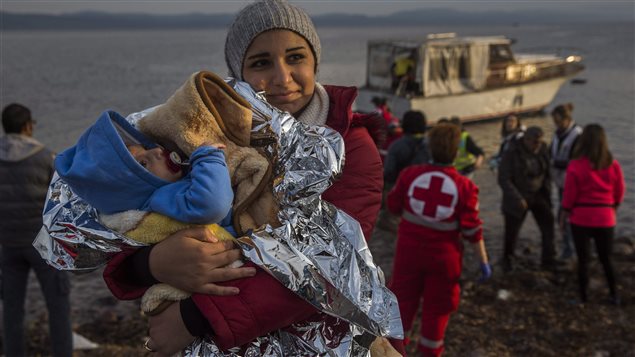 Une Syrienne débarque d'un petit bateau sur une plage grecque avec son bébé dans les bras.