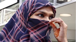 Zunera Ishaq talks to reporters outside the Federal Court of Appeal after her case was heard on whether she can wear a niqab while taking her citizenship oath, in Ottawa in September. We see a dark-eyed lady holding a plaid niqab at the midpoint of her nose. The rest of her face and hair are covered by the niqab.