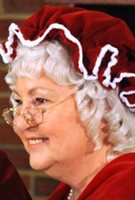 Mrs. Claus has white, curly hair under her red bonnet. Her granny glasses sit on the tip of her nose.