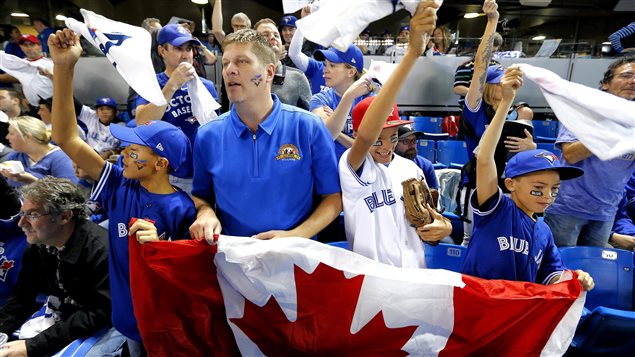Fans came out in force to support the Blue Jays last season. Will support sour if the team gets off to a slow start in 2016. We see a shot of fans of all ages, mostly male, holding a Canadian flag as they cheer from the stands. Most are dressed in Blue Jays blue.