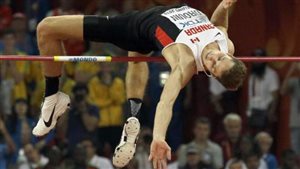 Derek Drouin needed a jumpoff against two other competitors to win the gold medal in Beijing. We see Drouin his head and left arm past the bar and his legs spread on the other side of the bar. He is coiled and ready to go over.