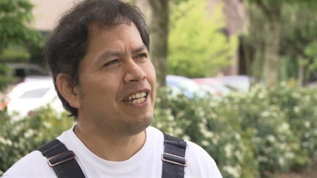 On his 49th birthday, Jose Figueroa is finally free. We see a dark-skinned man with brown hair and a gentle face standing in front of some greenery. He is looking off into the distance with his mouth slightly agape. We see the straps of his overalls over a white tee shirt.