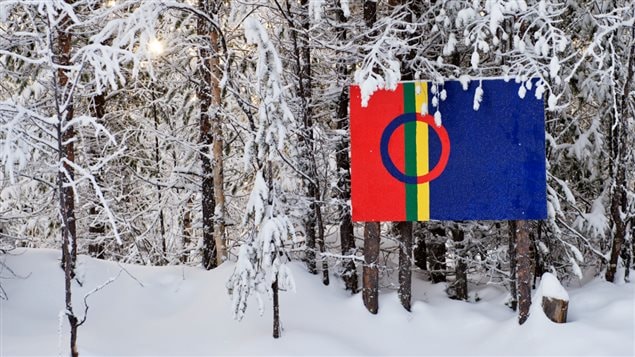 A red, green, yellow and blue Saami flag hangs in a snowy forest. (
