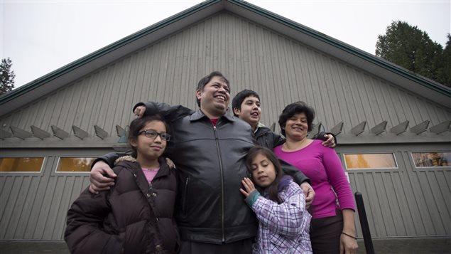 Jose Figueroa stands outside the Walnut Grove Lutheran Church with his family, left to right, Esmeralda, Ruby, Jose and wife Ivania in Langley, B.C. on Wednesday. We see Figueroa standing in the midst of his family. He and his wife are smiling widely.The children look just a tad nervous and kids tend to be when their picture is being taken. The family is sharing big hugs as his youngest daughter (to Figueroa's left) appears to be holding on to him for dear life.