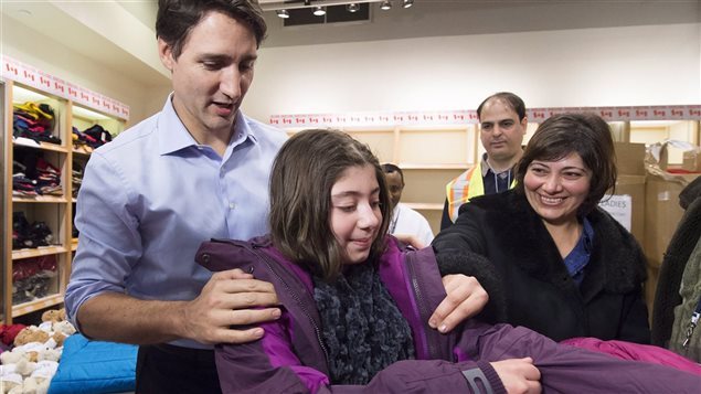 Justin Trudeau le pone un abrigo de invierno a una joven refugiada siria.