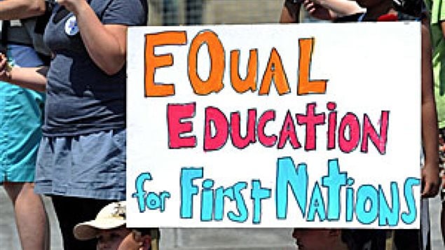 Aboriginal students in ten B.C. provincial districts are graduating less than 50 percent of the time, even though the provincial goal has set a graduation goal of 85 per cent. We see students holding a sign that says "Equal Education for First Nations." The lettering is orange red and light blue.