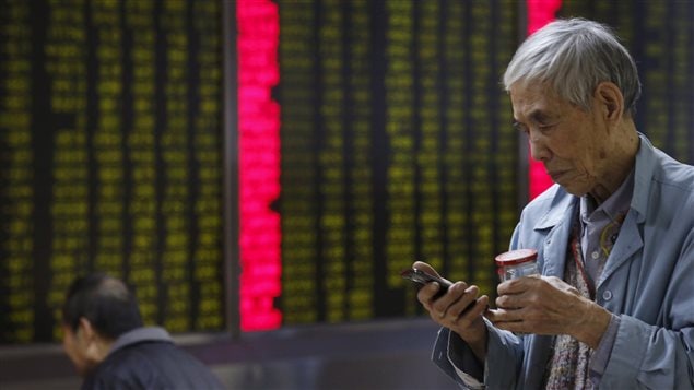 مستثمر ينظر إلى هاتفه المحمول أمام لوحة إلكترونية تعرض أسعار الأسهم في شركة وساطة مالية في العاصمة الصينية بكين يوم أمس.